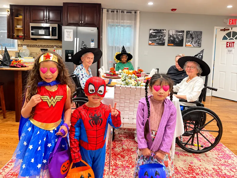 Children in Halloween costumes visiting residents who are wearing witch hats.